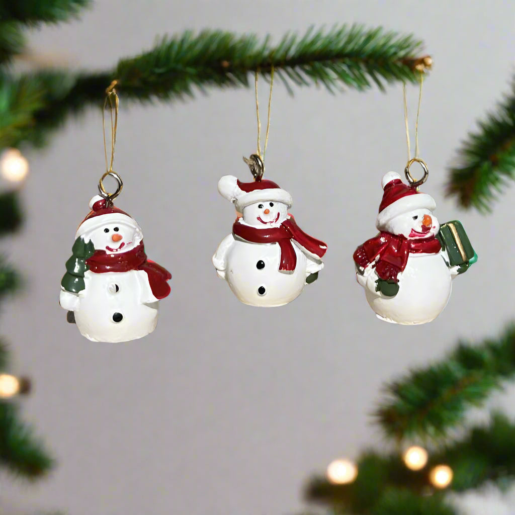 Three small snowman ornaments hanging from a fir branch