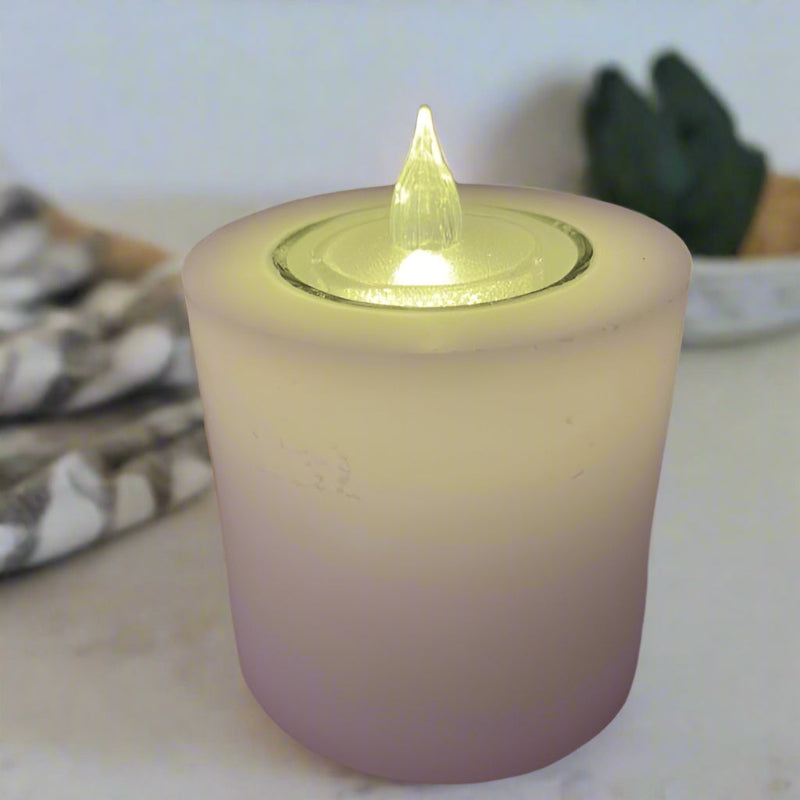 A white candle with a built-in glass holder and a flameless LED tealight