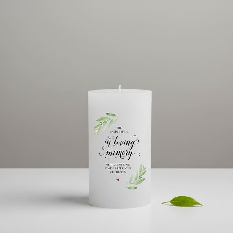 A white pillar candle with elegant black script and green watercolor leaf illustrations.