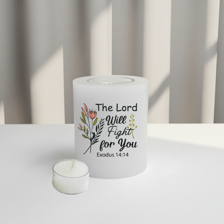 A white candle with a printed Christian scripture design reading 'The Lord Will Fight for You Exodus 14:14' alongside floral illustrations, set on a white surface with soft window light and vertical blinds in the background.