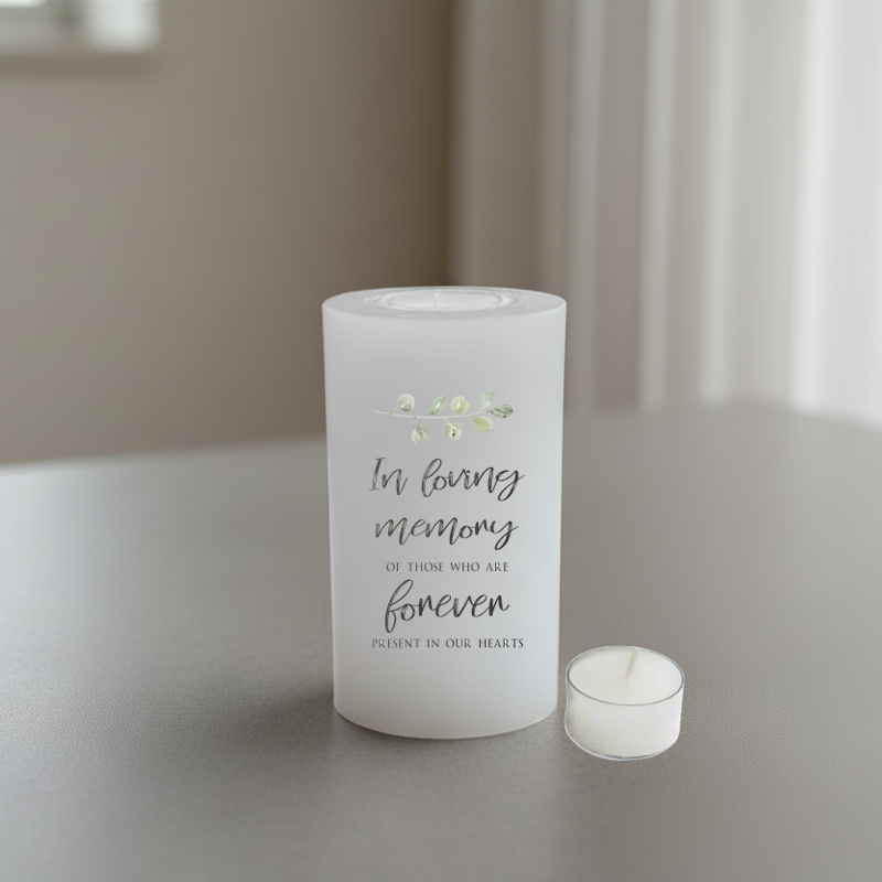 A white pillar candle printed with memorial text, placed on a grey surface.