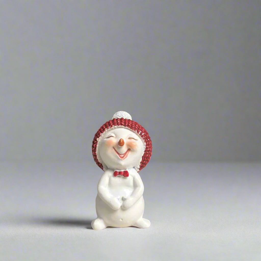 Small white snowman figurine with a red beanie and bow tie on a neutral background