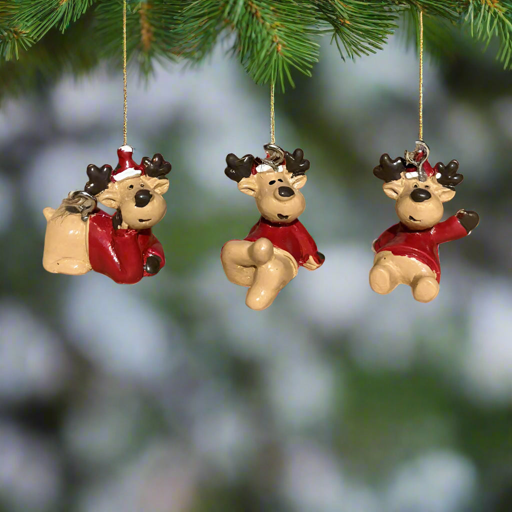 Three small reindeer figurines with red outfits hanging from a fir branch