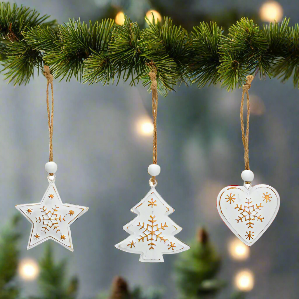 Three white Christmas ornaments shaped like a star, tree, and heart with gold snowflake designs on a white background.