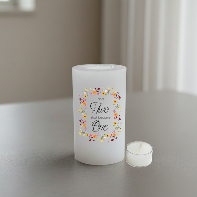 A white candle with a floral wreath design and the text 'and Two shall become One' in black script.