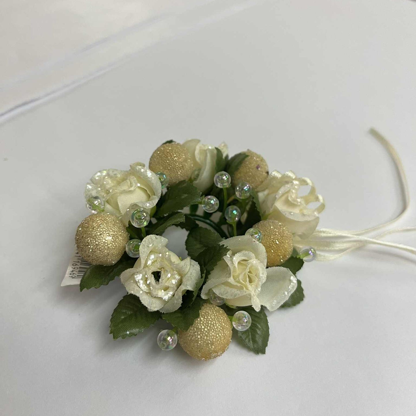 candle wreath of artificial flowers with gold balls and creme roses on a white surface