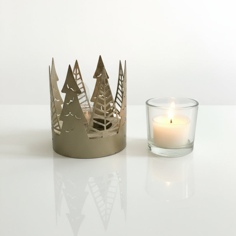 Decorative candle holder with tree cutouts next to a lit candle on a white surface