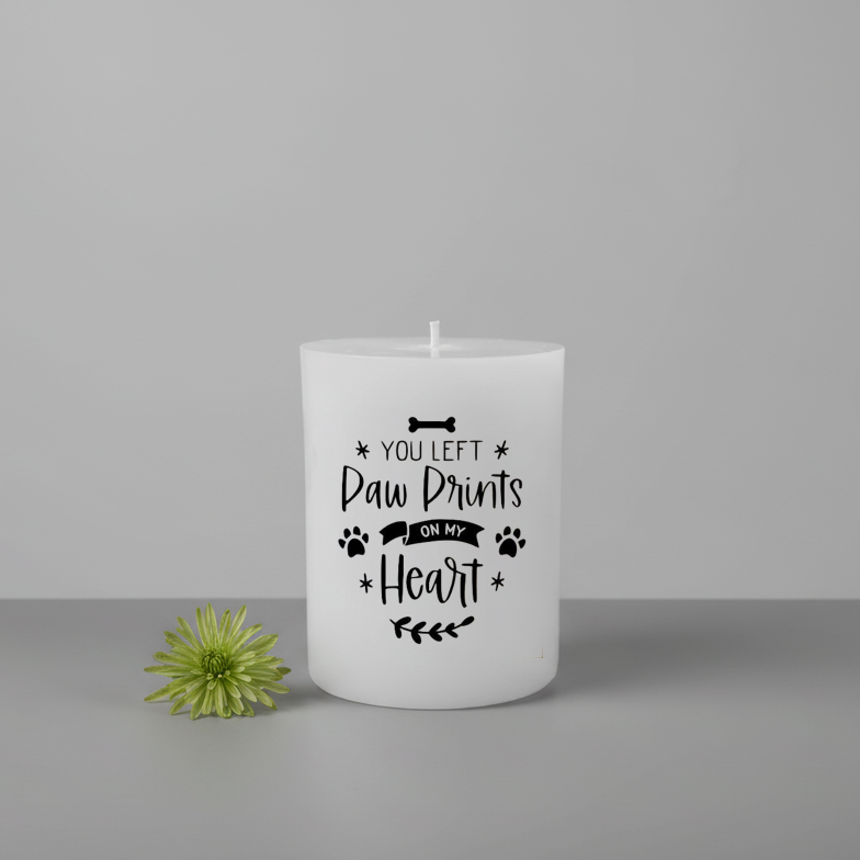 White candle with text 'You left paw prints on my heart' on a gray background