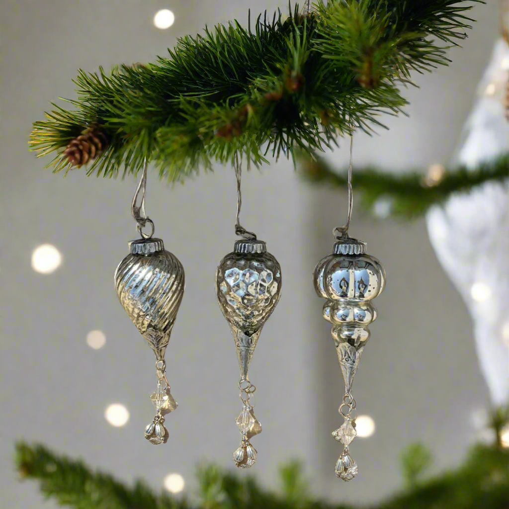 three silver vintage glass ornaments hanging on a christmas tree