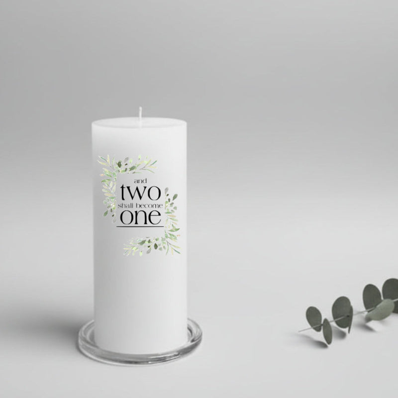 White wedding candle with 'and two shall become one' text and greenery design on a gray background