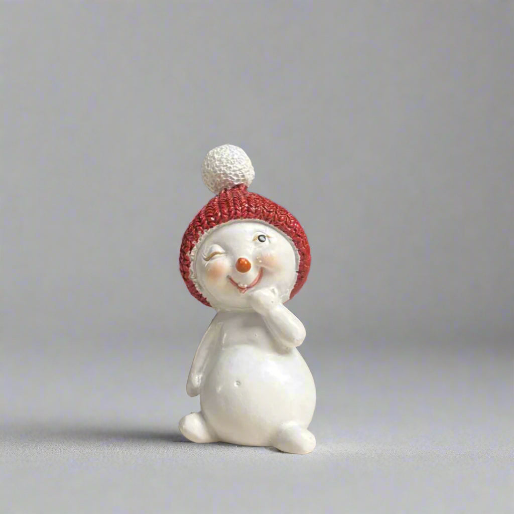 Small snowman figurine with a red beanie on a neutral background