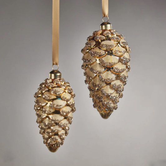 Two decorative pine cone ornaments with gold glitter on a gray background