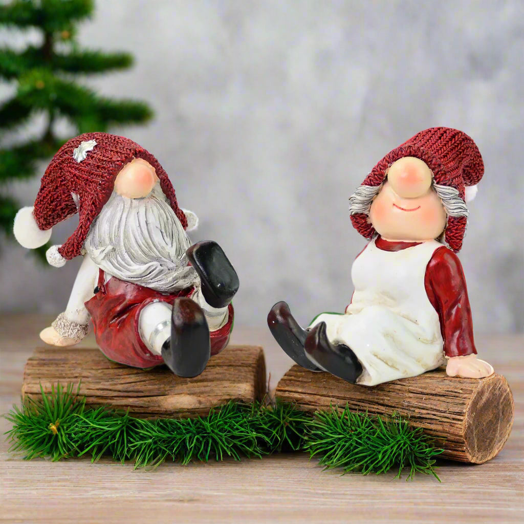 two gnome figurines with red hats sitting on a tree 