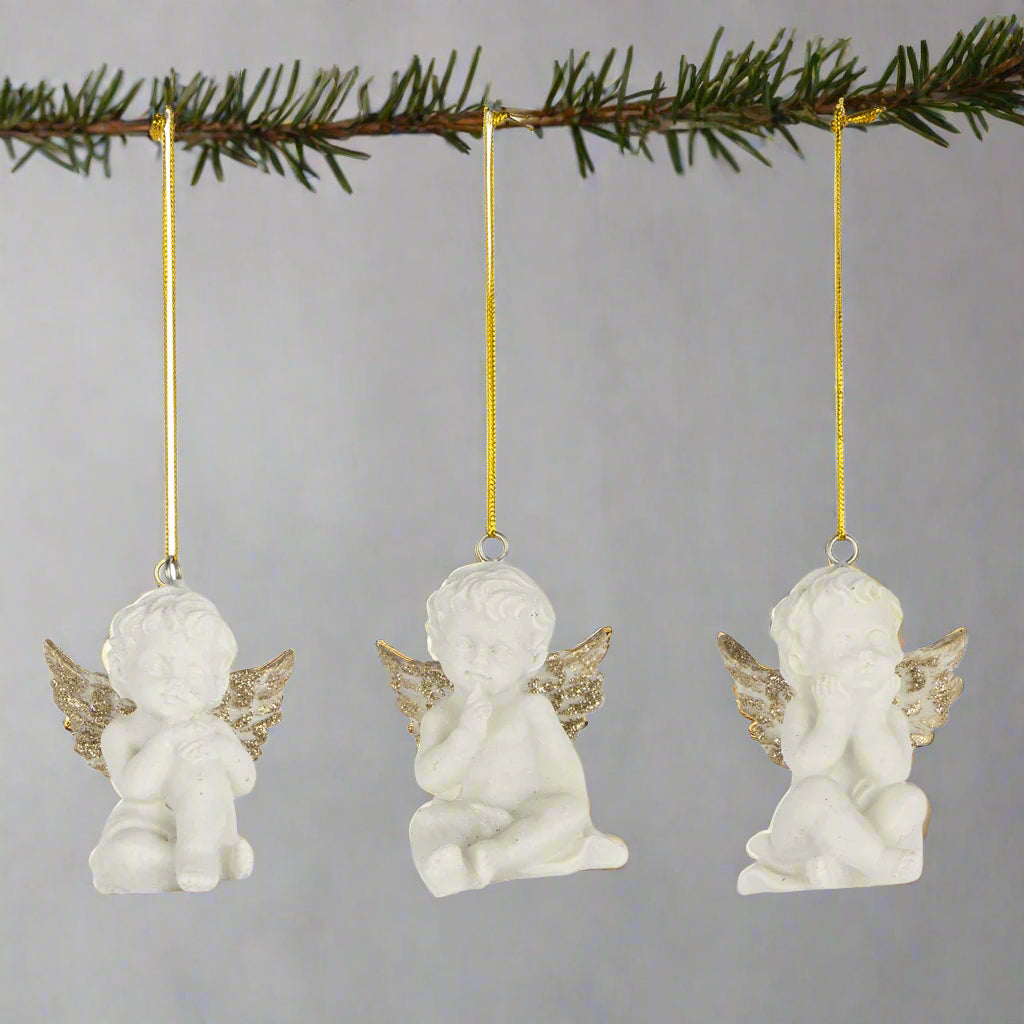 three angel ornaments with gold wings hanging on a fir branch