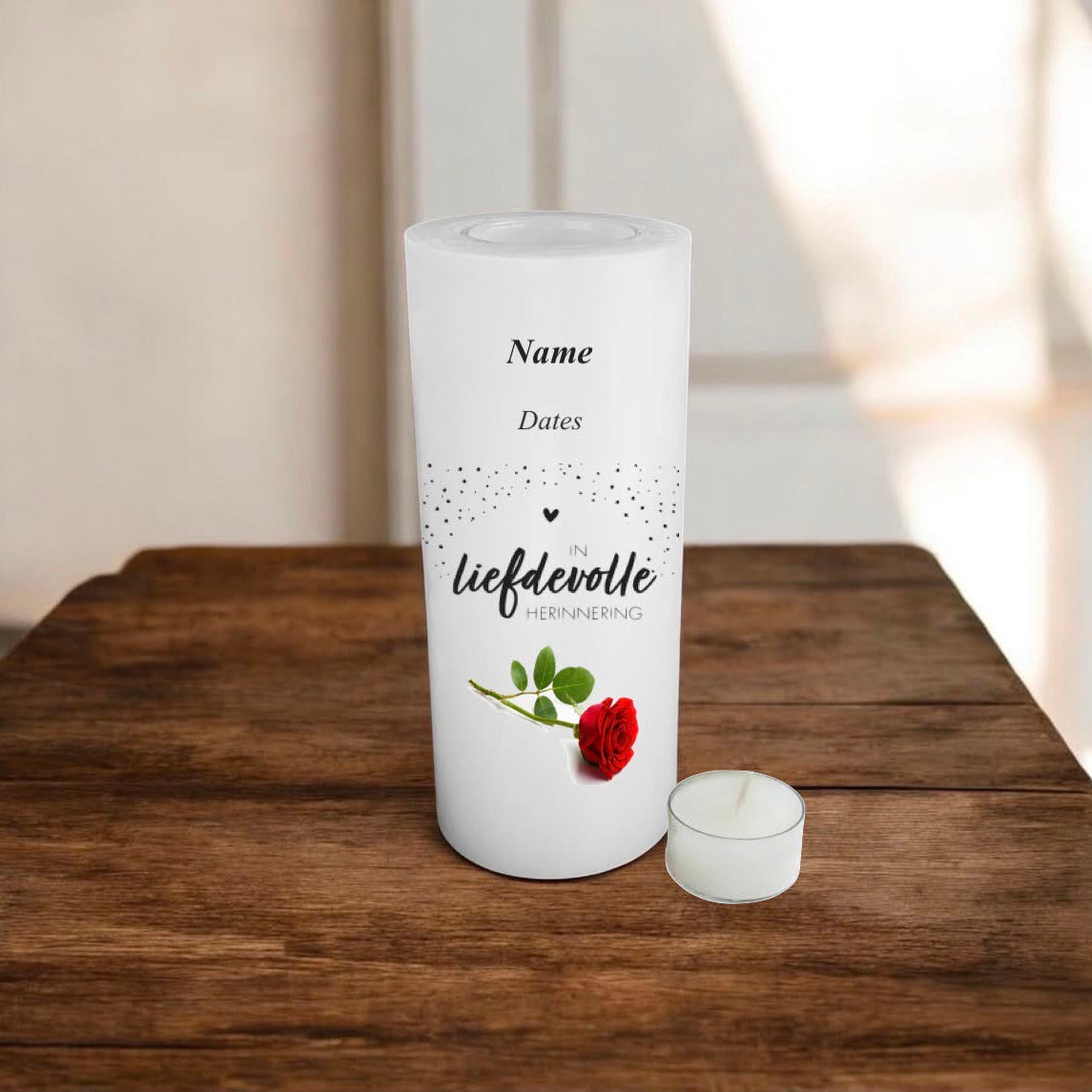 A white candle standing on a wooden table, printed in Afrikaans, and a red rose with green leaves.