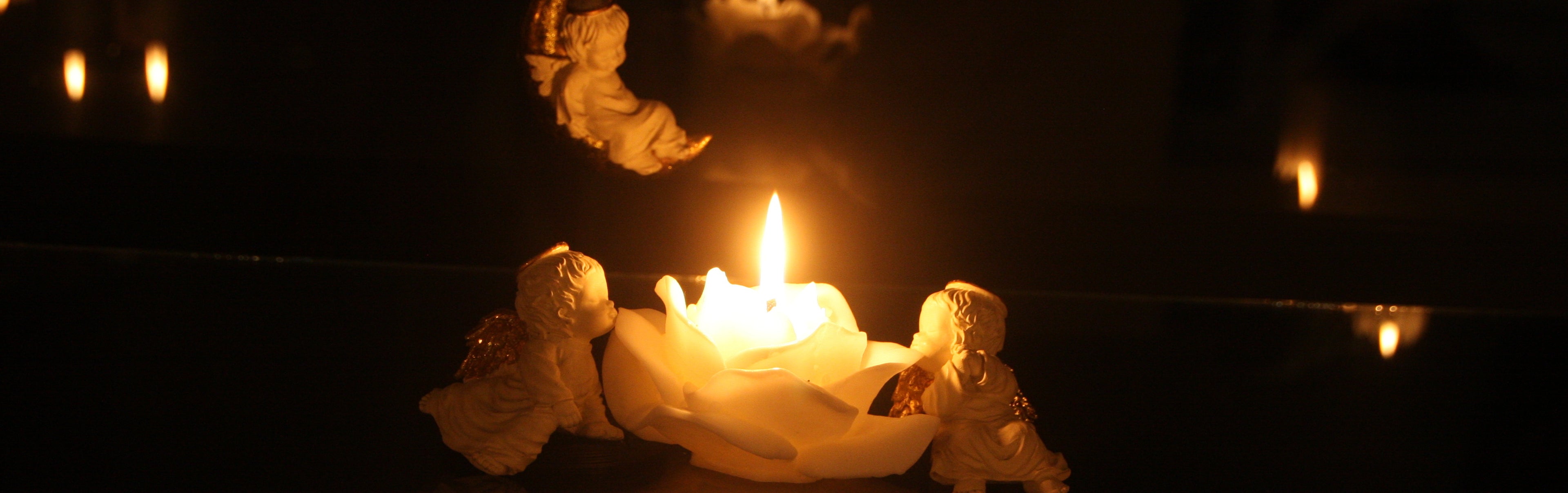 Candle with angel figurines on a reflective surface with a dark background