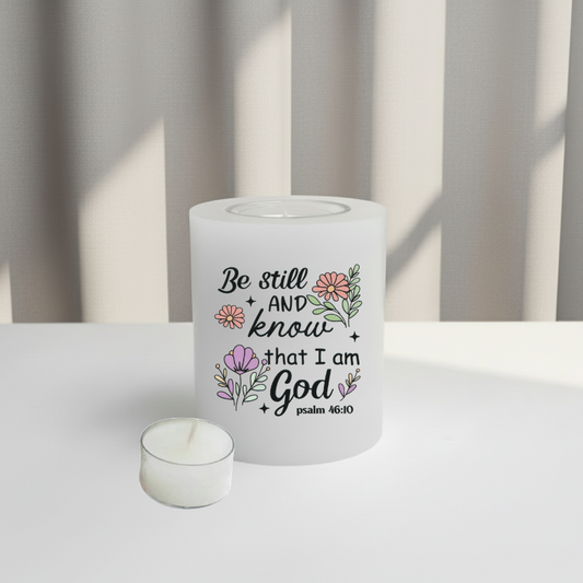 A white candle with a printed Bible verse and floral illustrations, sitting on a white surface with a soft-focus background of vertical blinds.