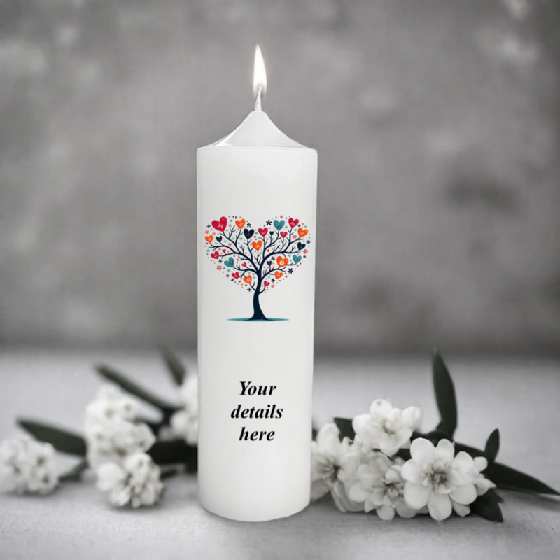 White belltop candle with a colorful heart tree design and space for text, surrounded by white flowers on a gray background.