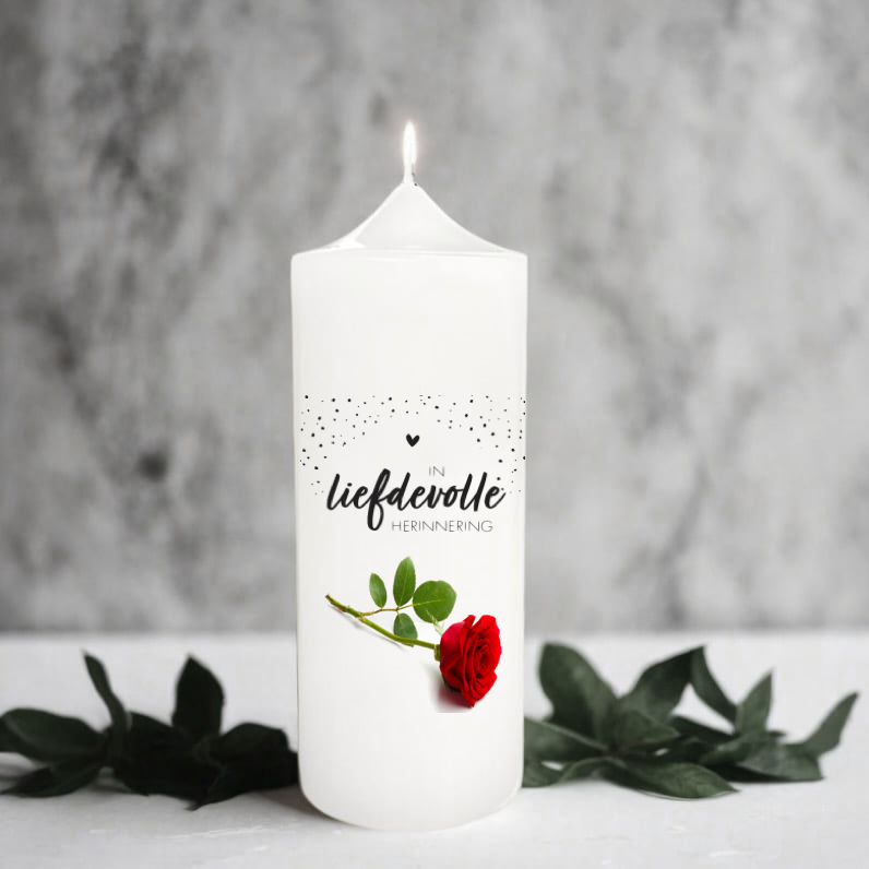 White memory candle with a red rose and afrikaans text on a grey background with green leaves