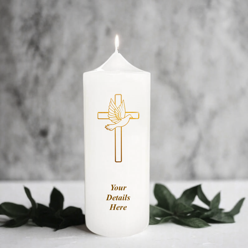 White candle with a gold cross and dove design, surrounded by greenery on a marble surface.