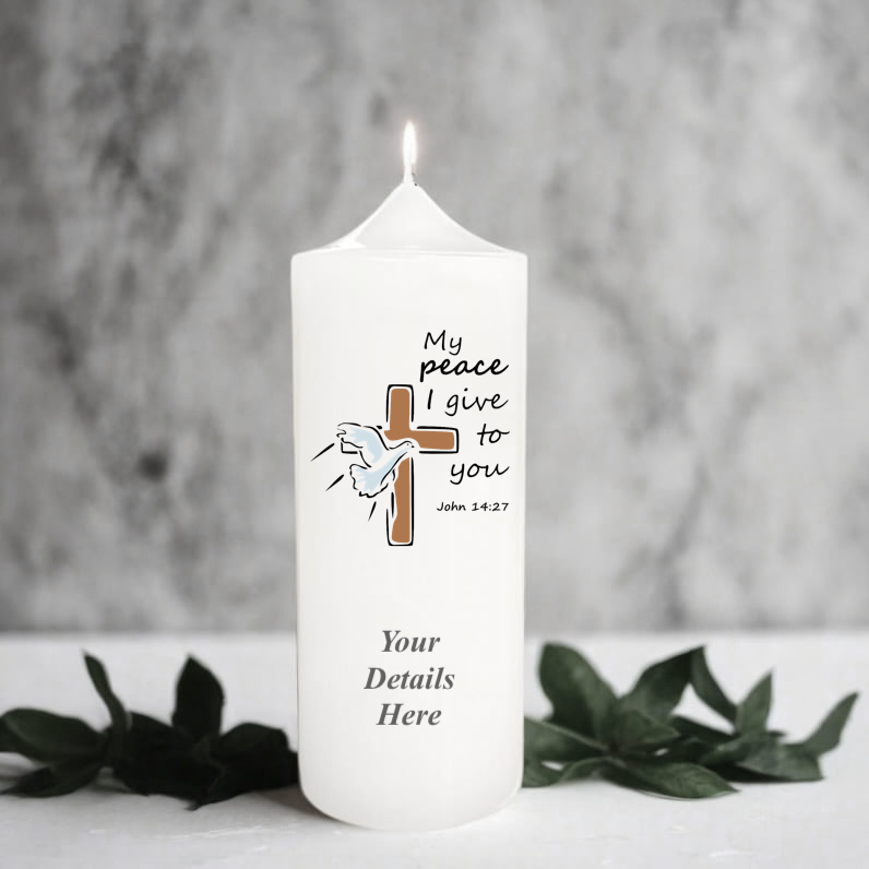 A white pillar candle with a lit flame, featuring a printed brown cross, A dove, and the text 'My peace I give to you John 14:27' 