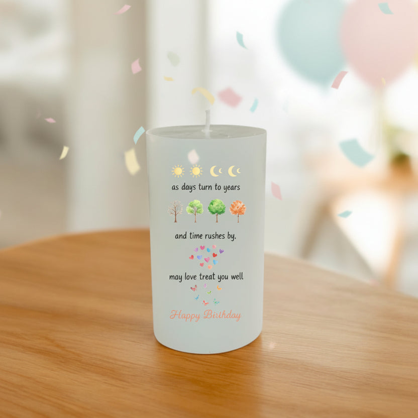 A white pillar candle with a printed birthday wish message, placed on a wooden table