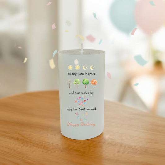 A white pillar candle with a printed birthday wish message, placed on a wooden table