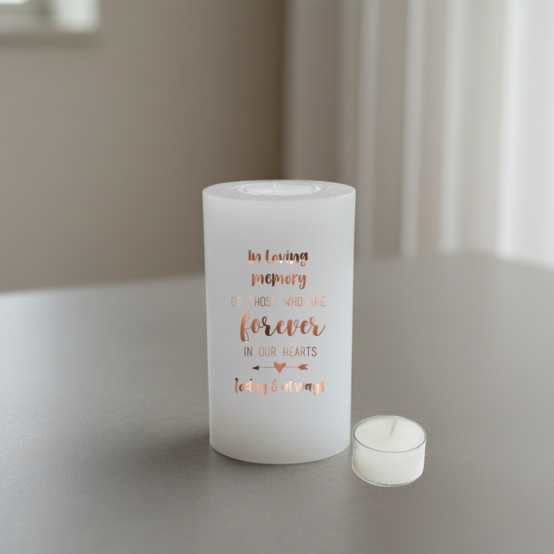 white candle with brown memorial text, placed on a grey surface.