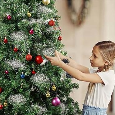 Child decorating a Christmas tree with ornaments and angels hair