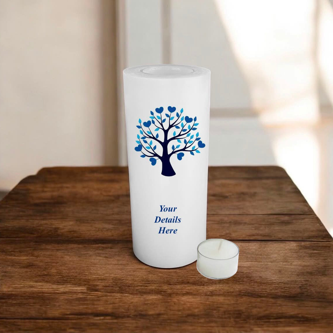 White candle with blue tree design and 'Your Details Here' text on a wooden surface.