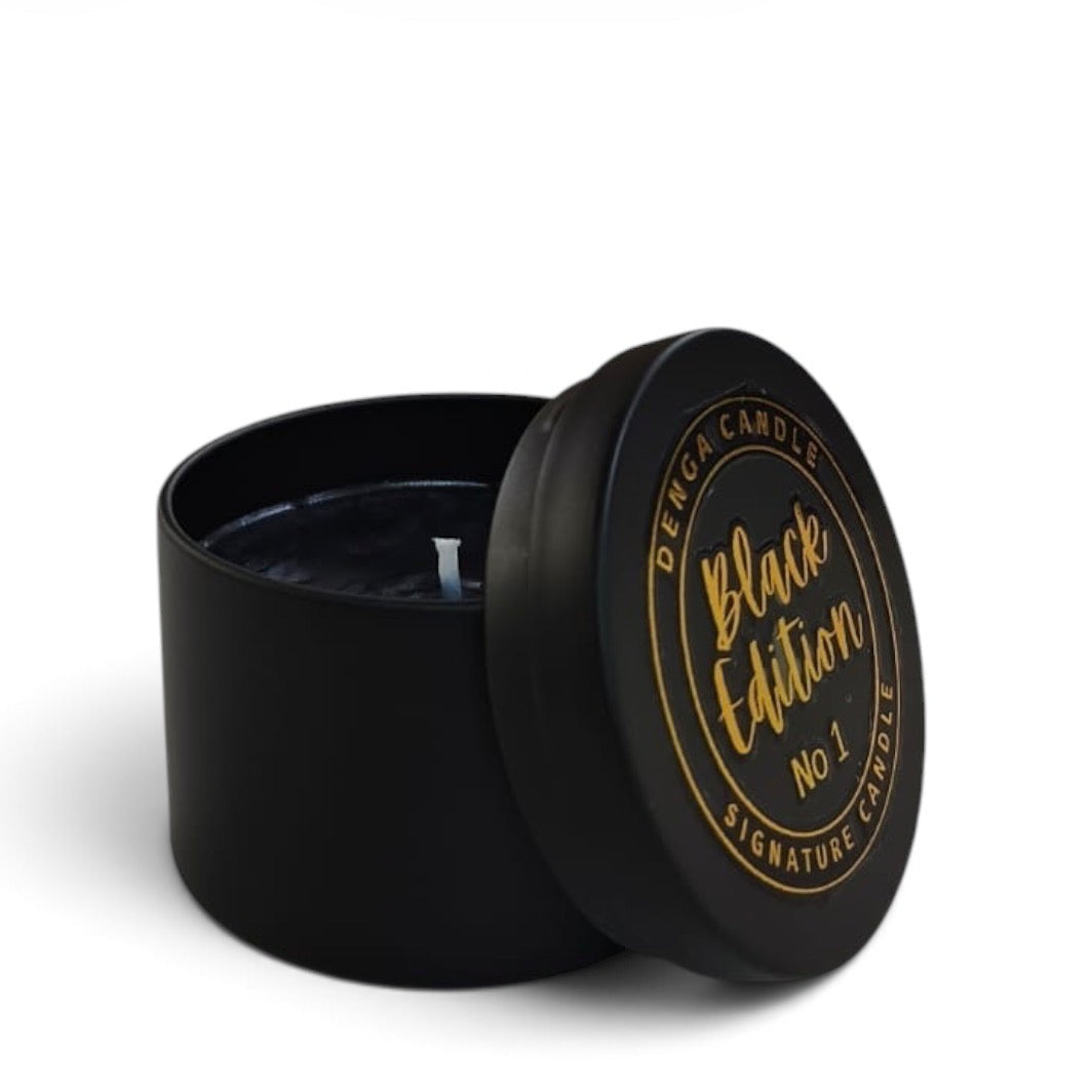 A black round candle tin with its lid leaning against the container, showing a black wax surface and gold printed text reading 'Black Edition No 1' and 'Denga Candle Signature Candle' on a white background.