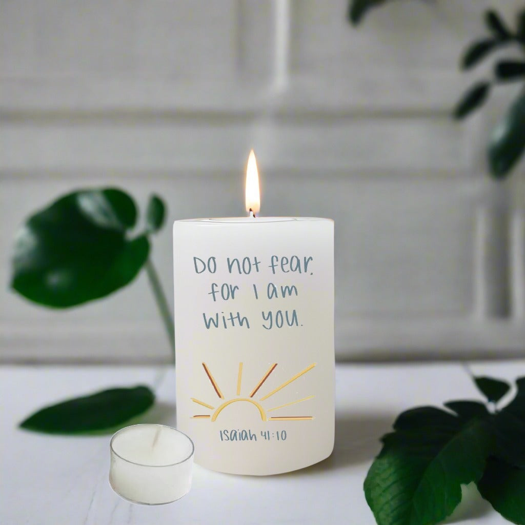 Candle with a motivational quote on a white surface with green leaves in the background