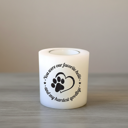 White candle with black text and paw print design on a wooden surface