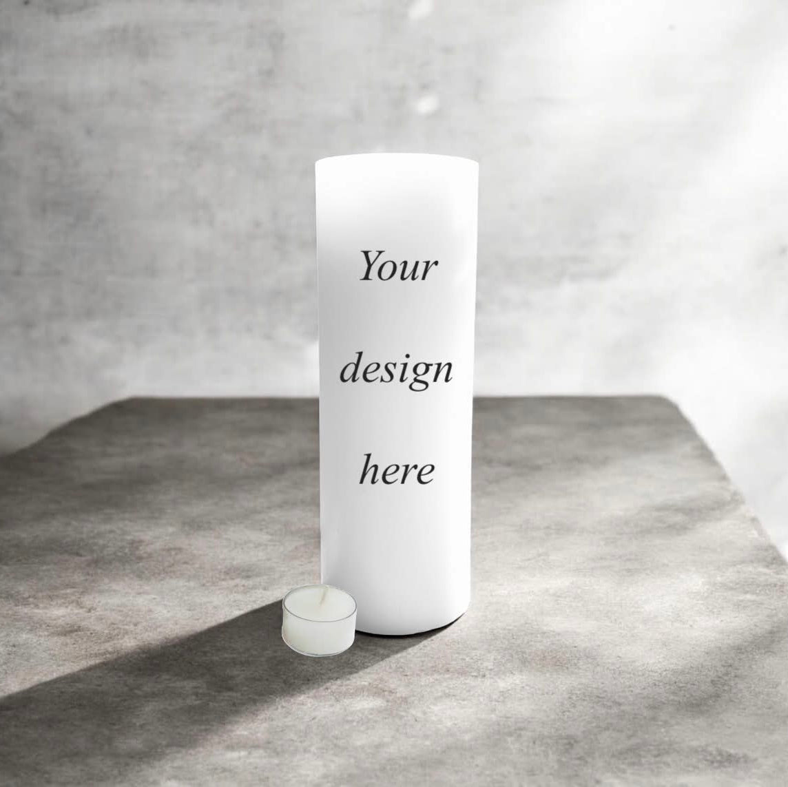 A white candle with the placeholder text 'Your design here' printed on the front, standing on a textured grey surface.