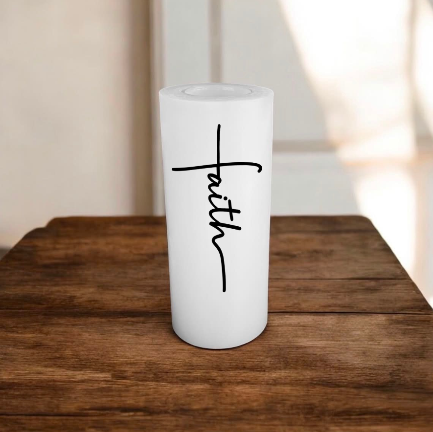White candle with text 'faith', placed on a wooden surface.