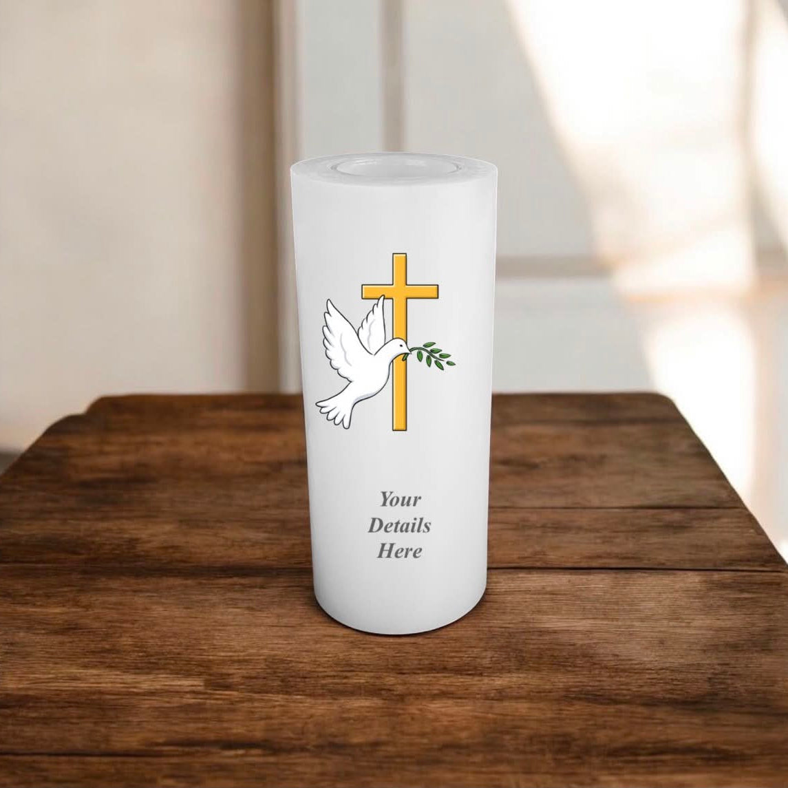 A white candle with cross, dove, and olive branch design on a wooden surface.