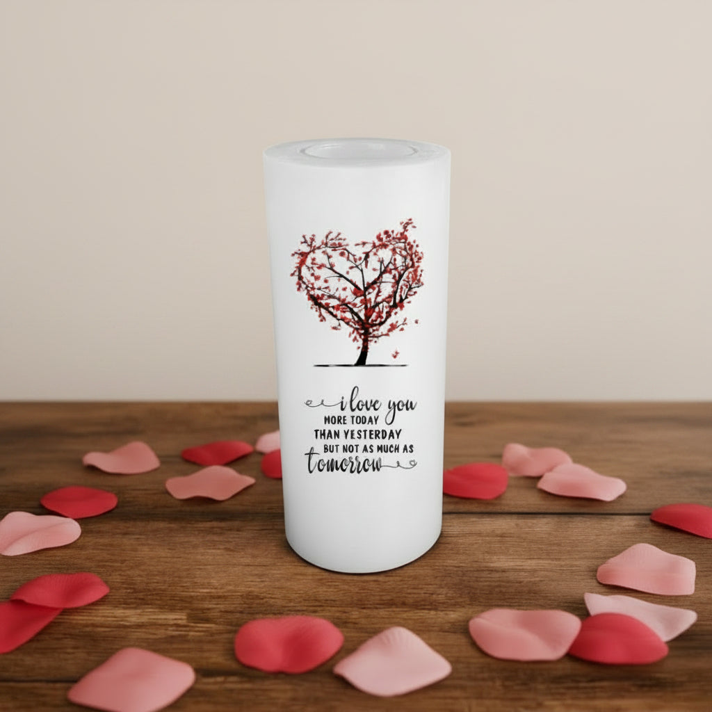 A white candle featuring a red heart-shaped tree design and the printed message 'I love you MORE TODAY THAN YESTERDAY BUT NOT AS MUCH AS tomorrow'.