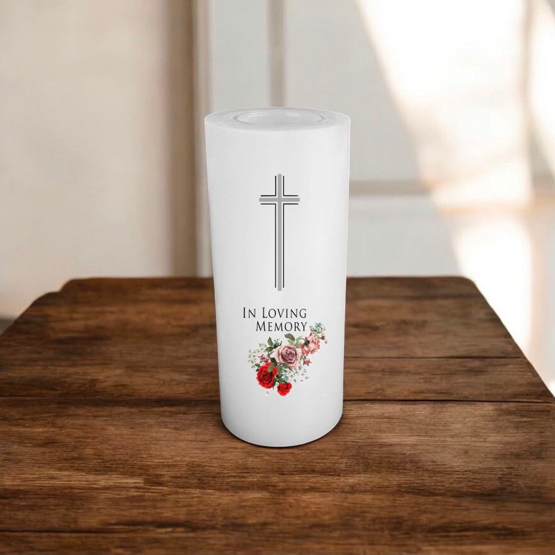 White candle printed with a cross, text and roses, placed on a wooden surface