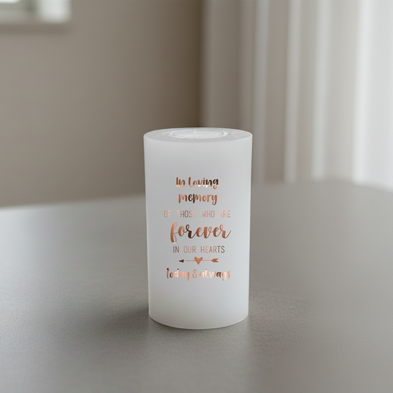 white candle with brown memorial text, placed on a grey surface.