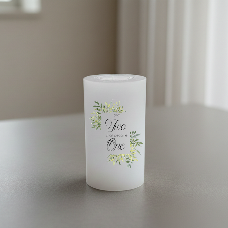 A white candle with a floral wreath design and the words 'and Two shall become One' in black script.