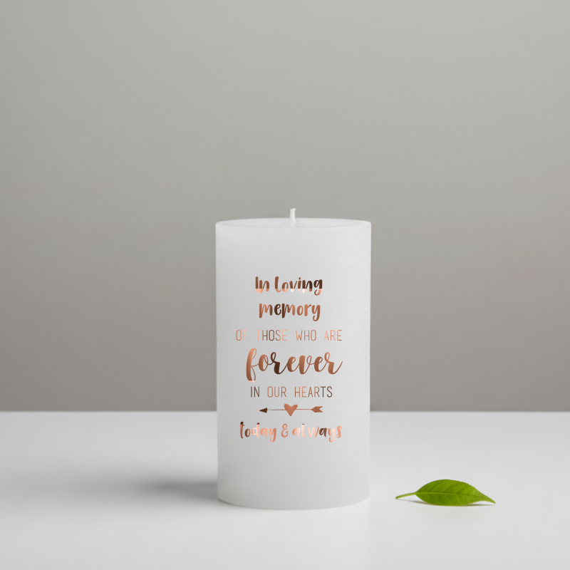 white candle with brown memorial text, placed on a grey surface.