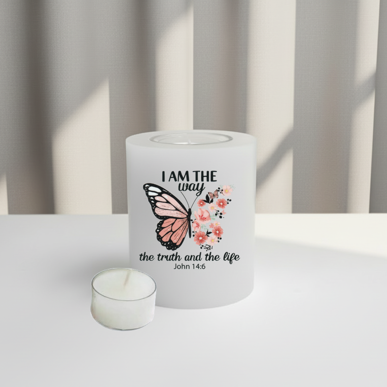 A white candle holder with a printed design featuring a butterfly, pink flowers, and the text 'I AM THE way the truth and the life John 1:4' on a white surface
