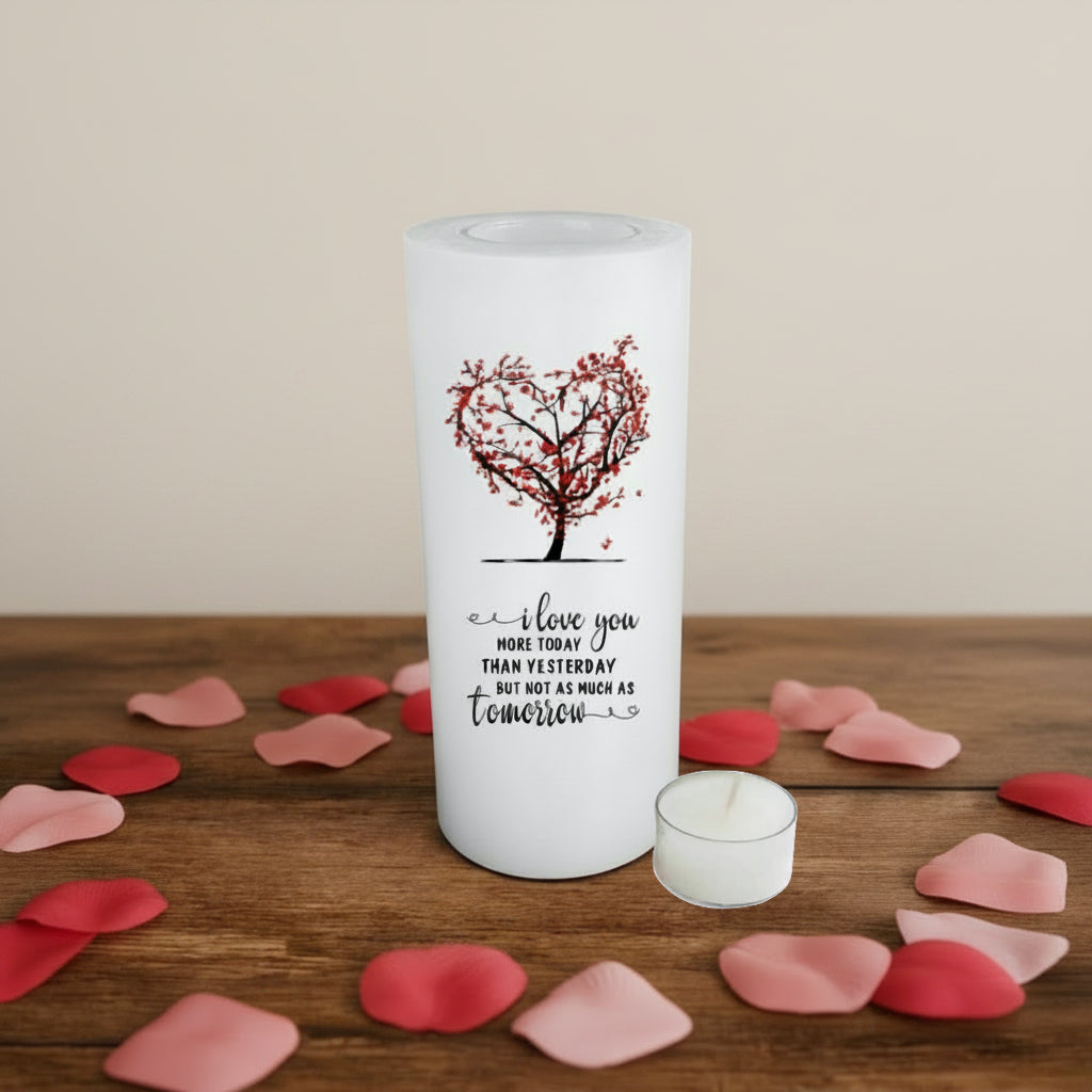 A white candle featuring a red heart-shaped tree design and the printed message 'I love you MORE TODAY THAN YESTERDAY BUT NOT AS MUCH AS tomorrow'.