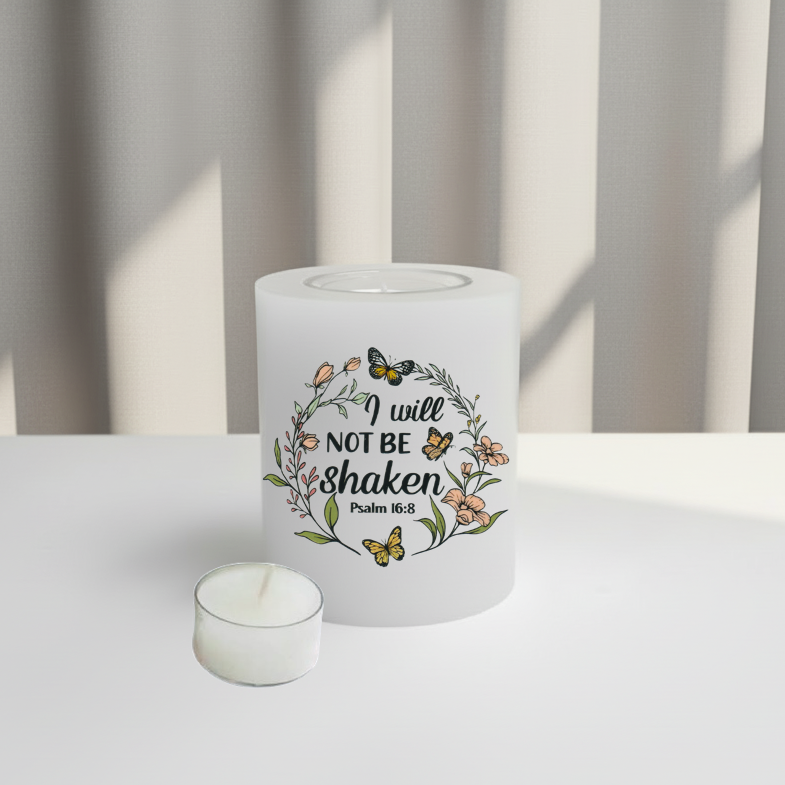 A white candle featuring a printed graphic of a floral wreath with butterflies and the text 'I will NOT BE shaken Psalm 16:8'. 