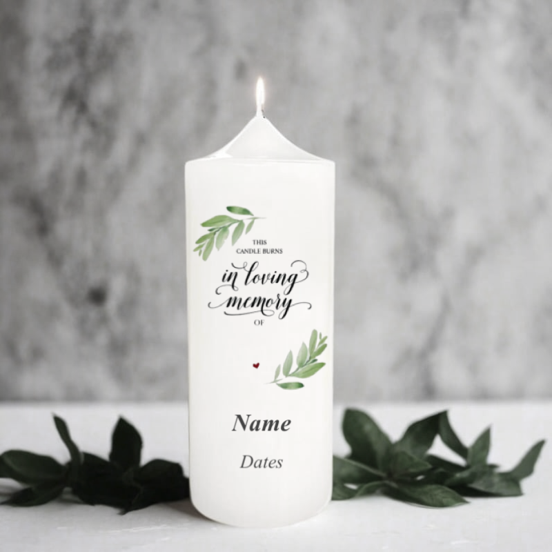 White memory candle with text and green leaves on a gray background