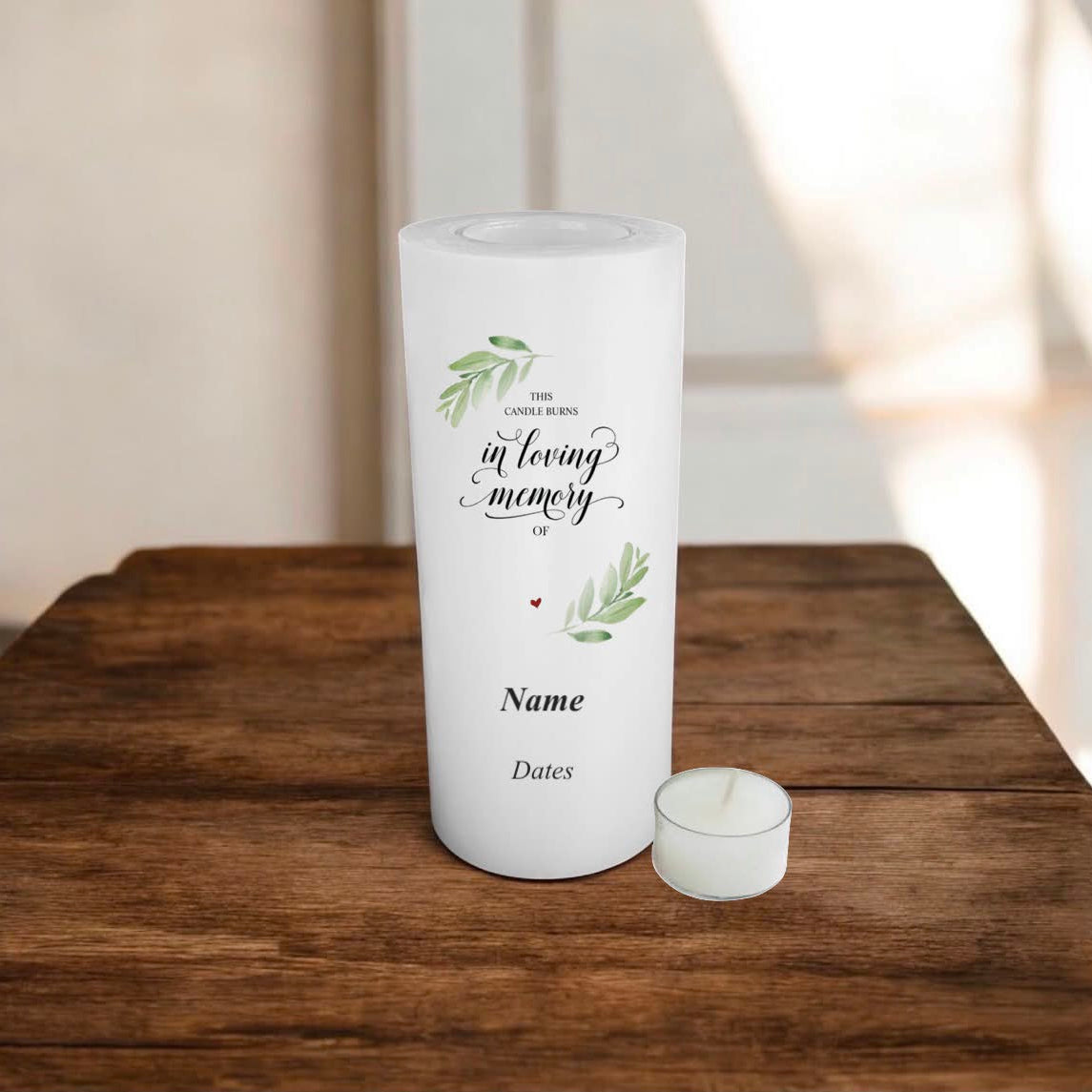 White candle with memory text and green leaves branch design on a wooden surface.
