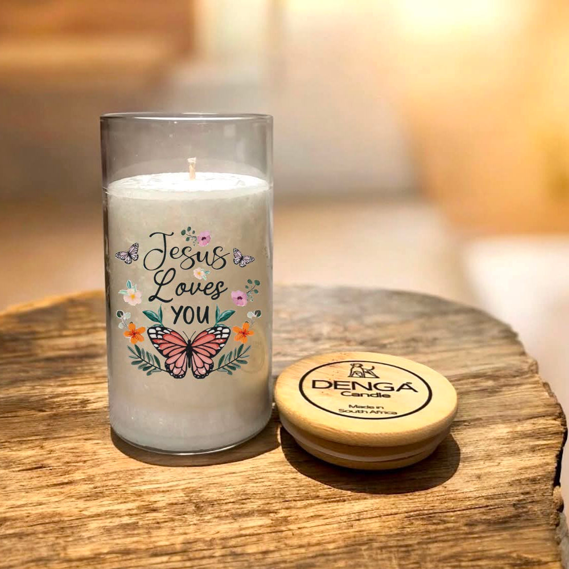 A glass jar candle with white wax and a printed design reading 'Jesus Loves You' round wooden lid 