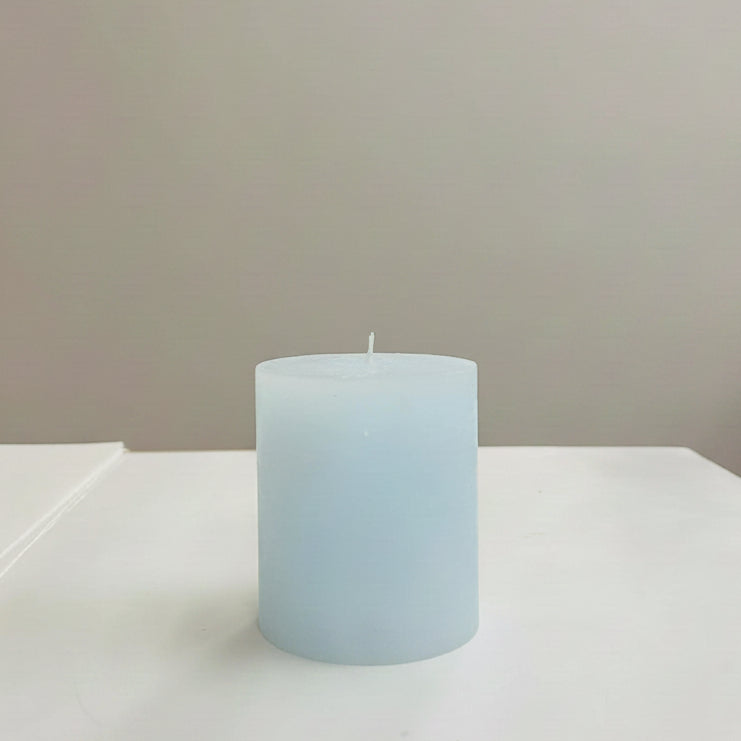 Light blue candle on a white surface with a neutral background