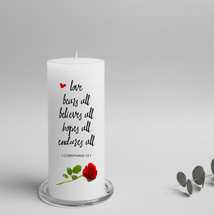 A white pillar candle with a text and a rose, placed on a glass plate holder