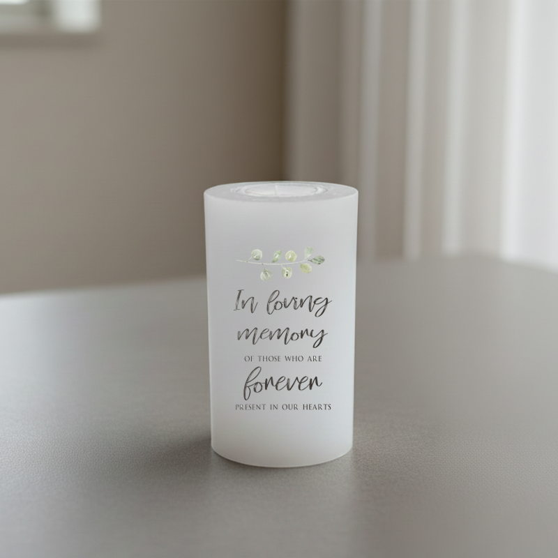 A white pillar candle printed with memorial text, placed on a grey surface.